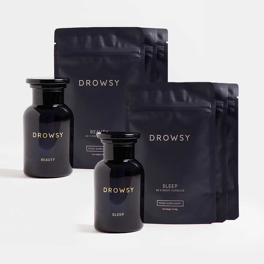 Two dark jars and four black pouches from drowsysleepco’s Supplements – Sleep & Glow Protocol are arranged on a white background. Both the jars and pouches are labeled “Beauty” and “Sleep,” and each contains a sleep supplement designed to support restorative rest and promote radiant skin.