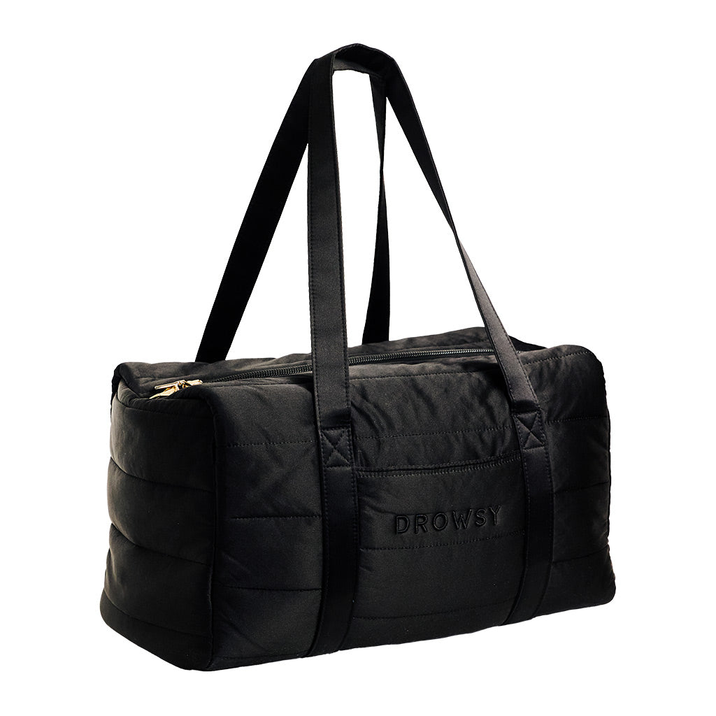 The Drowsy Silk Weekender - Black Jade by Drowsy is a quilted black duffel bag featuring two long handles, a zipper closure, and the word “DROWSY” embroidered on the side—perfect as a stylish weekend bag for your next getaway.