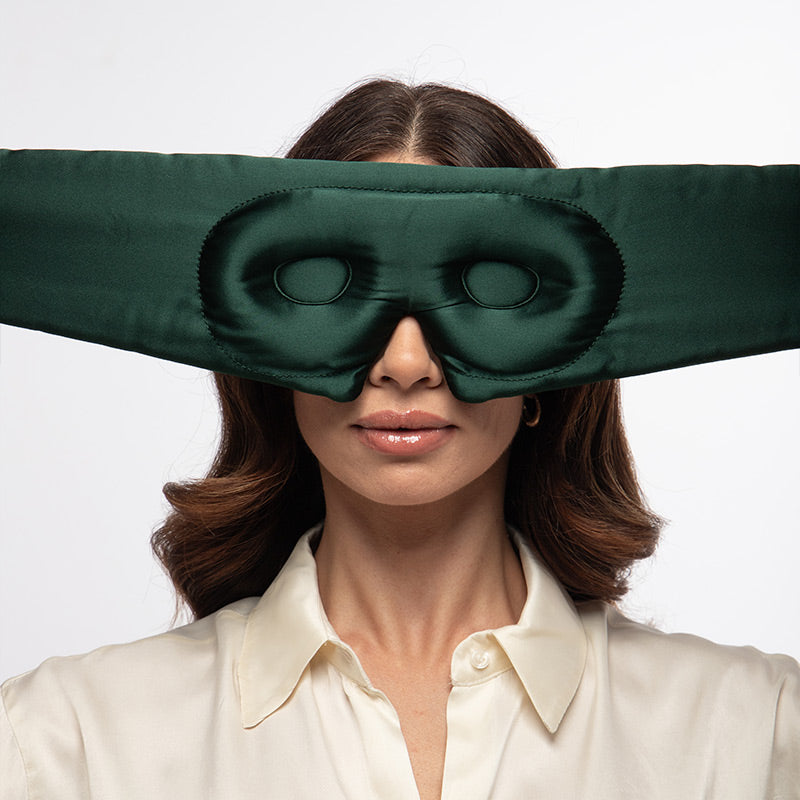 A person wears an Ivy Garden - Eyelash Protecting Mask, a wide, dark green sleep mask with contoured eyecups, over their eyes.