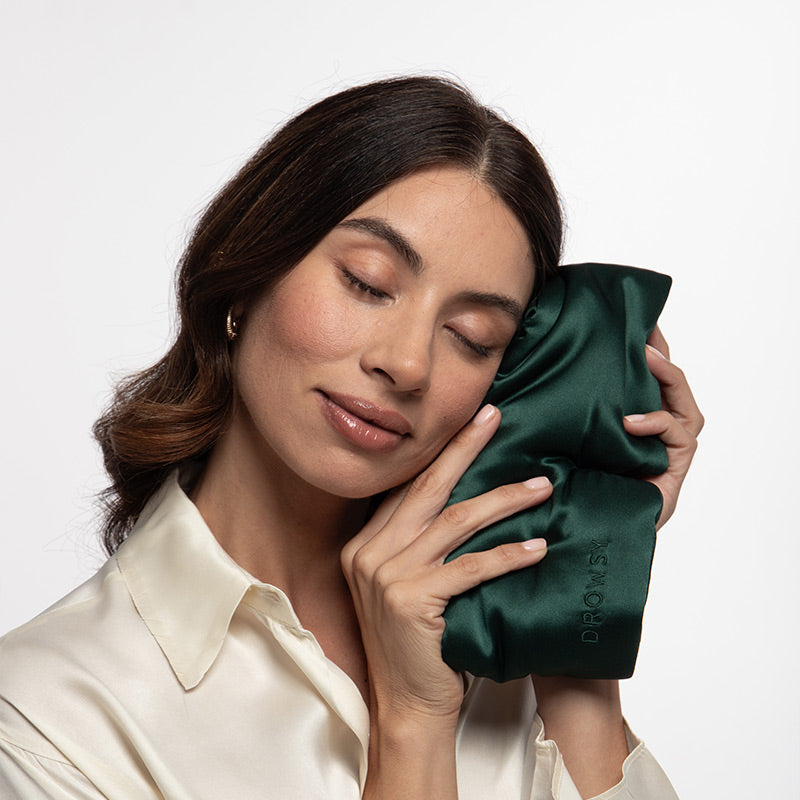 A woman with her eyes closed rests her cheek against a dark green silk Ivy Garden - Eyelash Protecting Mask with contoured eyecups.