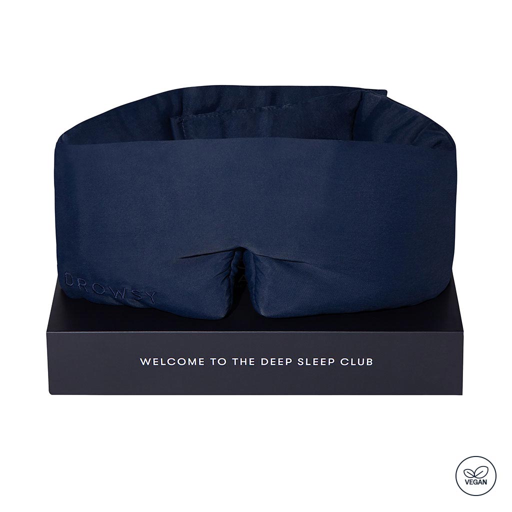 The Midnight Blue - Vegan Silk Sleep Mask by drowsysleepco features "drowsy" embroidered on the side and is displayed on a black box reading "Welcome to the Deep Sleep Club," with a vegan icon in the bottom right corner.