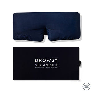 A navy blue drowsysleepco Midnight Blue - Vegan Silk Sleep Mask with "DROWSY" embroidery is shown above its matching box. A vegan icon appears in the bottom right corner.