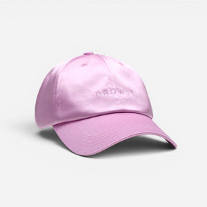 The Drowsy Silk Cap - Hotel Paradiso Heatwave by Drowsy is a light pink baseball cap with "DROWSY" embroidered on the front, offering stylish hair protection and shown against a plain white background.
