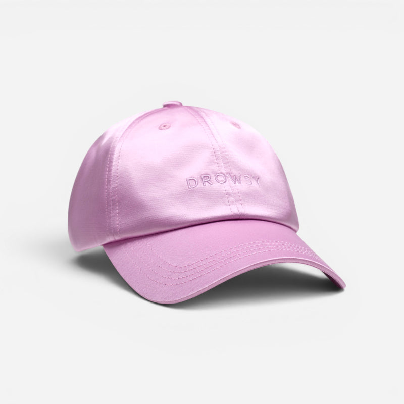 The Drowsy Silk Cap - Hotel Paradiso Heatwave by Drowsy is a light pink baseball cap with "DROWSY" embroidered on the front, offering stylish hair protection and shown against a plain white background.