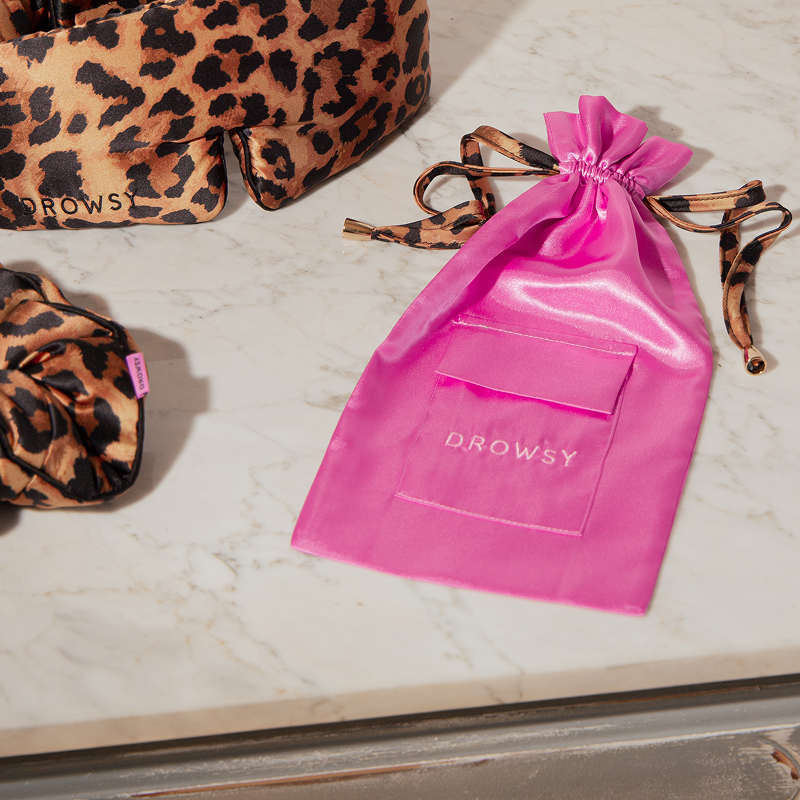 The Hotel Paradiso Carry Pouch by us.drowsysleepco rests on a marble surface beside two leopard-print silk eye masks—an elegant, restful travel accessory.