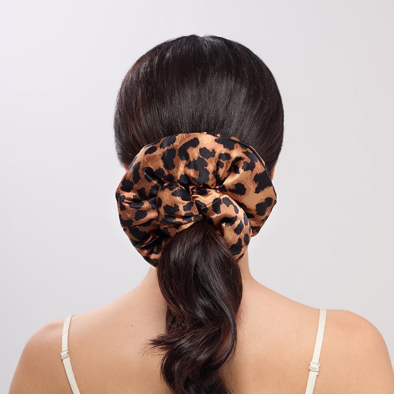 A woman with long dark hair in a low ponytail, secured by the Hotel Paradiso - Wild Thing Padded Scrunchie from us.drowsysleepco, wears a white thin-strap top while photographed from the back to subtly highlight her hair's thickness and style.