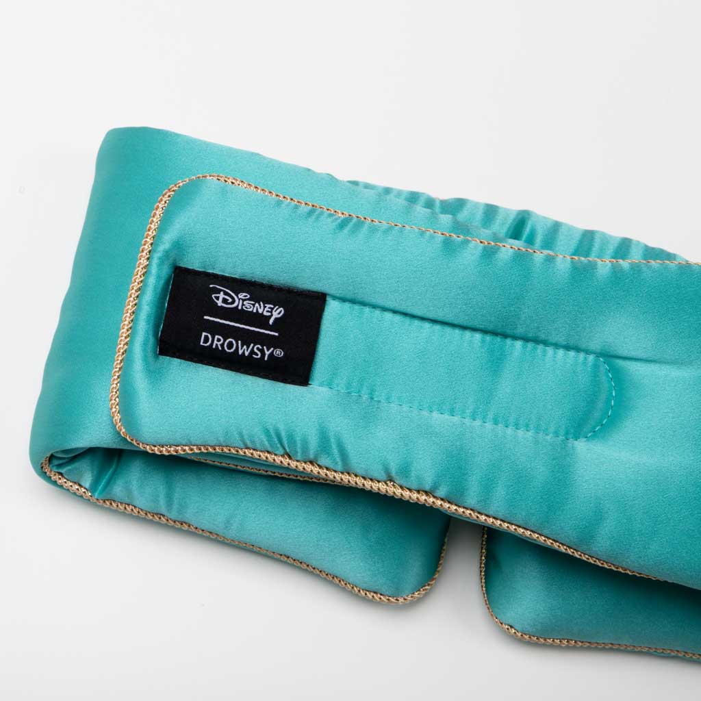 The Jasmine Sleep Mask by drowsysleepco is shown in teal satin with gold trim. A black label displays "Disney Drowsy" in white. The mask appears against a white background.
