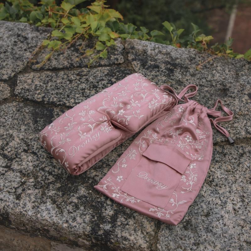 A pink floral Pride & Prejudice - Complete collection original mulberry silk sleep mask and matching drawstring pouch resting on a stone surface.