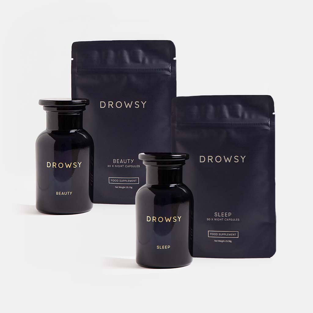 Two dark jars and two matching pouches labeled “drowsysleepco” with “Sleep & Glow Protocol” written on them are displayed against a simple light background. The sleek, minimalist packaging perfectly reflects the premium quality of this restorative sleep supplement and skin supplement duo.