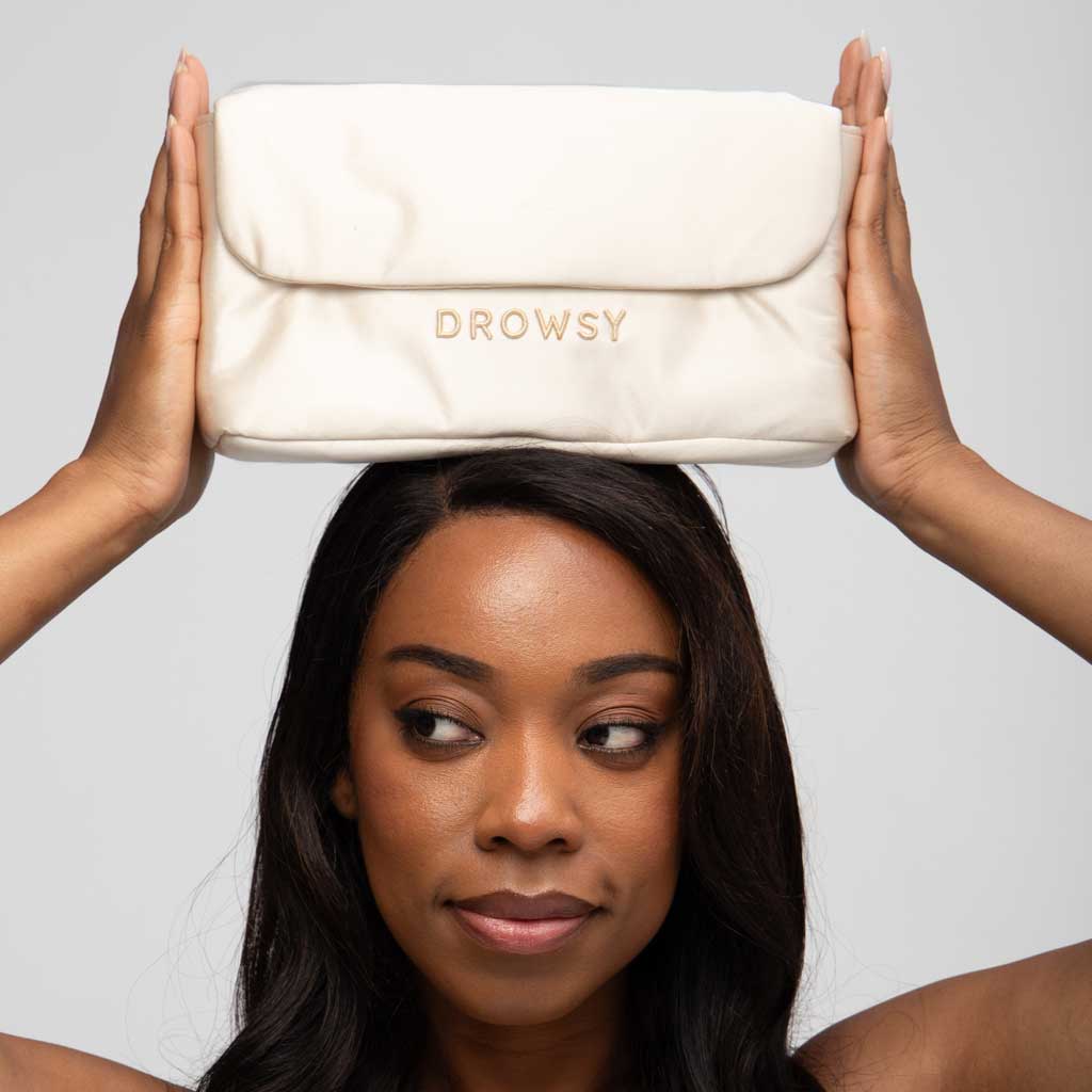 A woman holds the Perfect Escape Bundle - Dusty Gold by drowsysleepco on top of her head, looking down and to the side as if embracing beauty sleep, set against a plain light background.