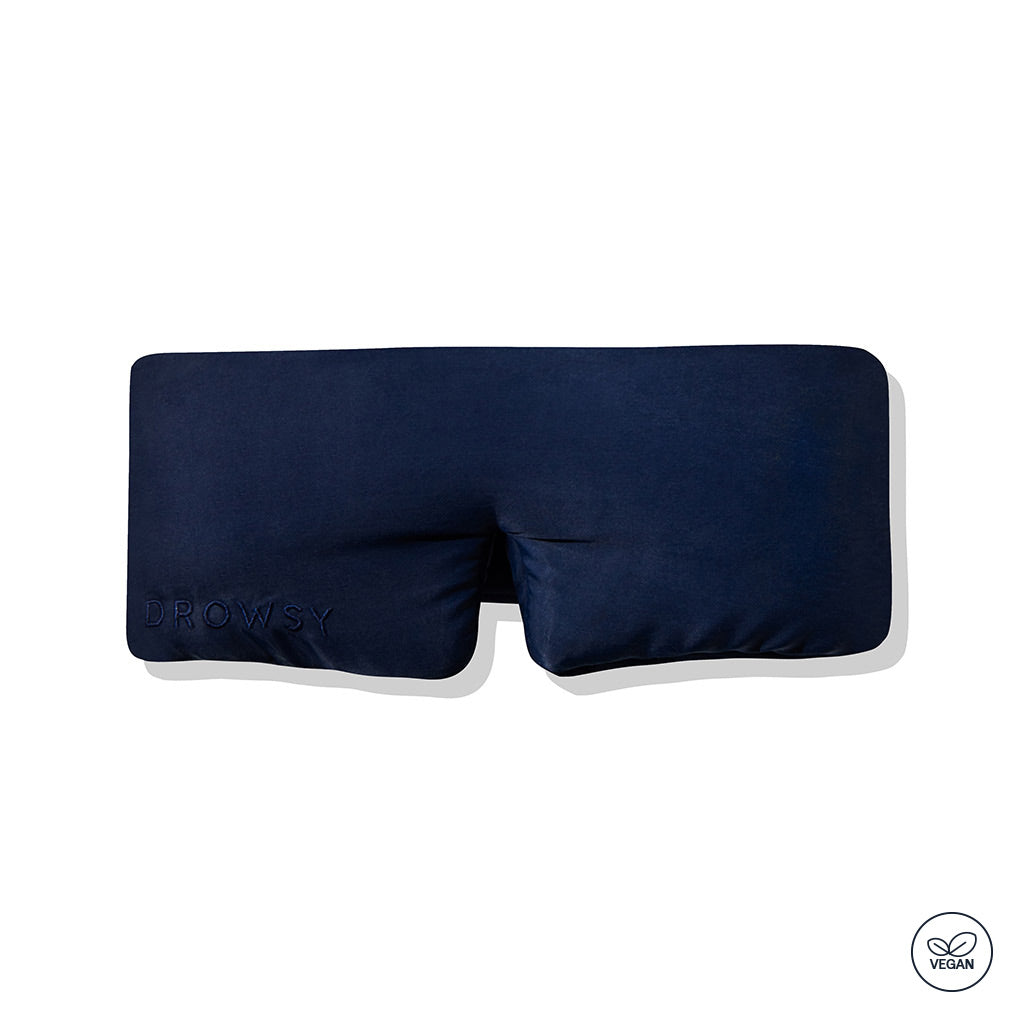 The Midnight Blue - Vegan Silk Sleep Mask by drowsysleepco is a dark blue rectangular mask with "DROWSY" embossed on the left side, a notched bottom design, and a vegan certification icon in the lower right corner.
