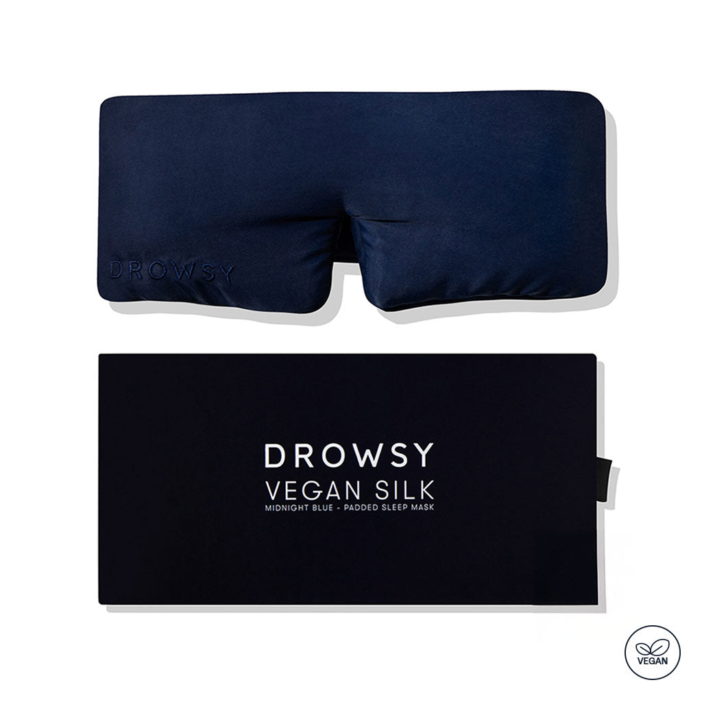 A navy blue drowsysleepco Midnight Blue - Vegan Silk Sleep Mask with "DROWSY" embroidery is shown above its matching box. A vegan icon appears in the bottom right corner.