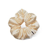 The Champagne Gold Padded Scrunchie by us.drowsysleepco features gathered, shiny satin in a cream-gold hue with a small black tag—ideal for adding hair volume.
