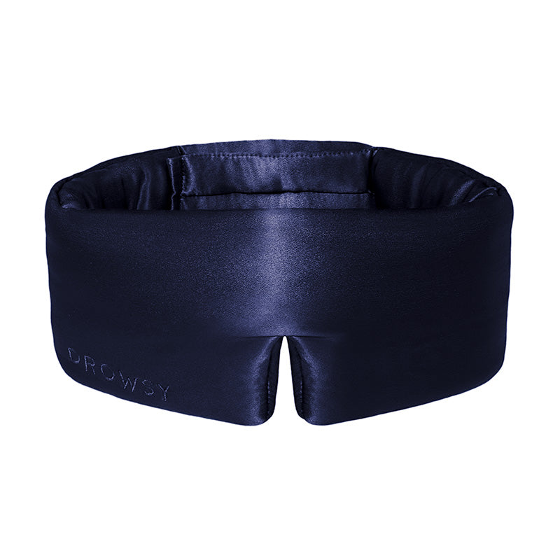 The Midnight Blue sleep mask by drowsysleepco features thick, padded sides and DROWSY embroidery on the front. Made from dark blue mulberry silk, it is designed to block out light completely for restful sleep.