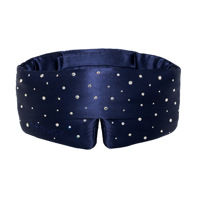 The Silk Sleep Mask Crystals by Swarovski® from drowsysleepco features navy blue silk, sparkling Swarovski® crystals for a starry effect, soft padding, blackout coverage, and DROWSY subtly embossed on the fabric.