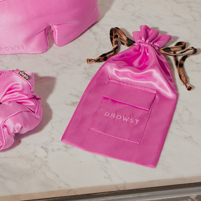 A Hotel Paradiso Carry Pouch from us.drowsysleepco sits on a marble surface next to a matching silk eye mask and scrunchie, forming an elegant and cozy travel accessory set.