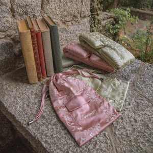 Two Pride & Prejudice - Complete collection original mulberry silk sleep masks and their matching drawstring pouches resting on a stone ledge next to a row of antique books.