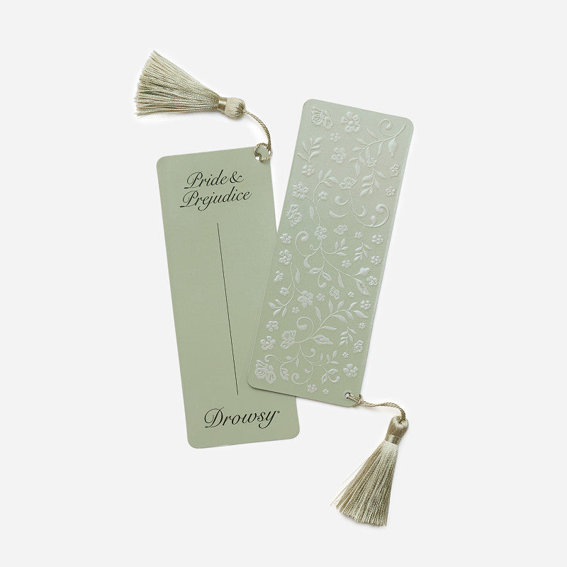 Two sage green bookmarks with tassels, one embossed with a floral pattern and the other featuring the text Pride & Prejudice, resting beside a Pride & Prejudice - Sage Eyelash Protecting Sleep Mask.